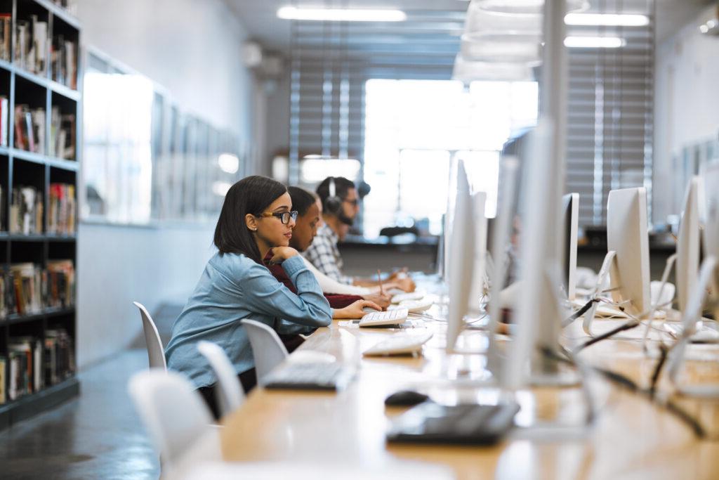 A group of university students working on computers in the library at campus